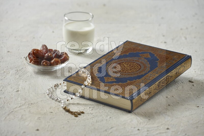 Quran with dates, prayer beads and different drinks all placed on textured white background