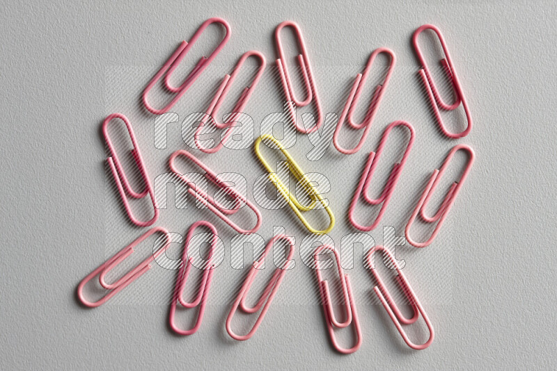A bunch of pink paper clips with a different colored paper clip in the center on grey background