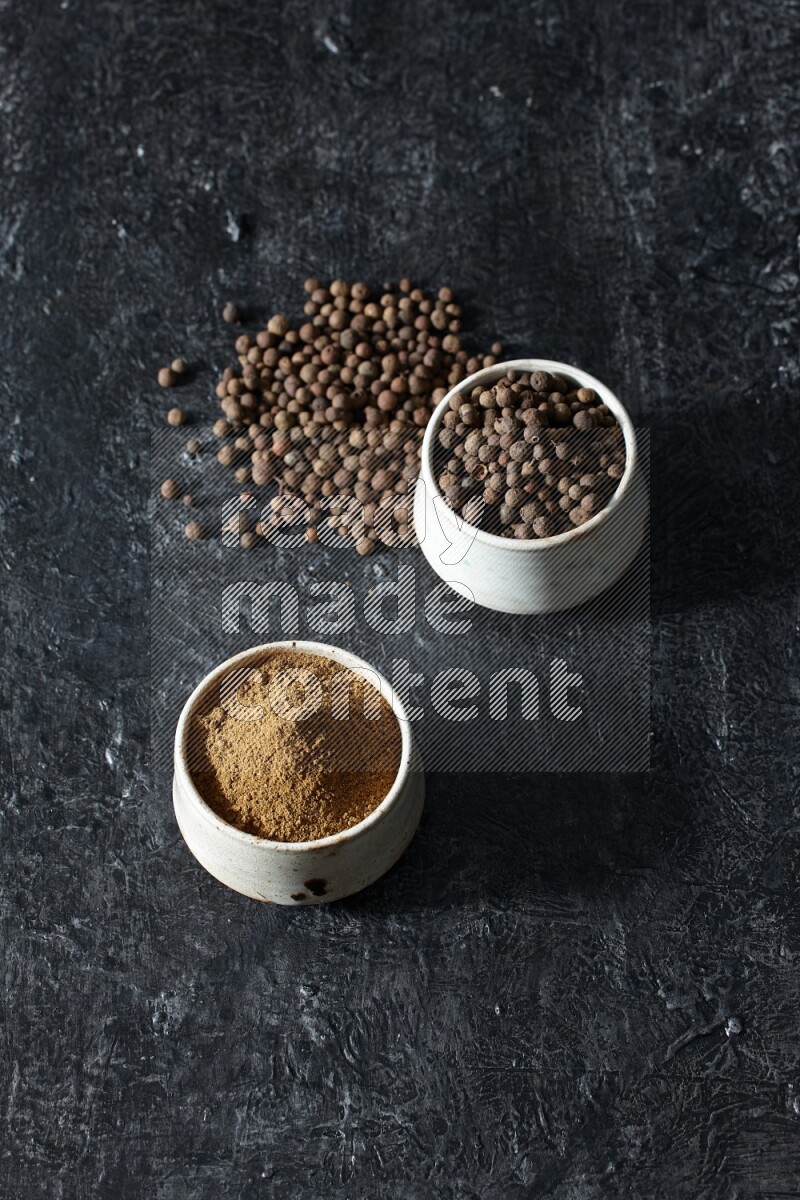 2 beige bowls, one full of allspice powder and the other full of whole balls and both spread on a textured black flooring