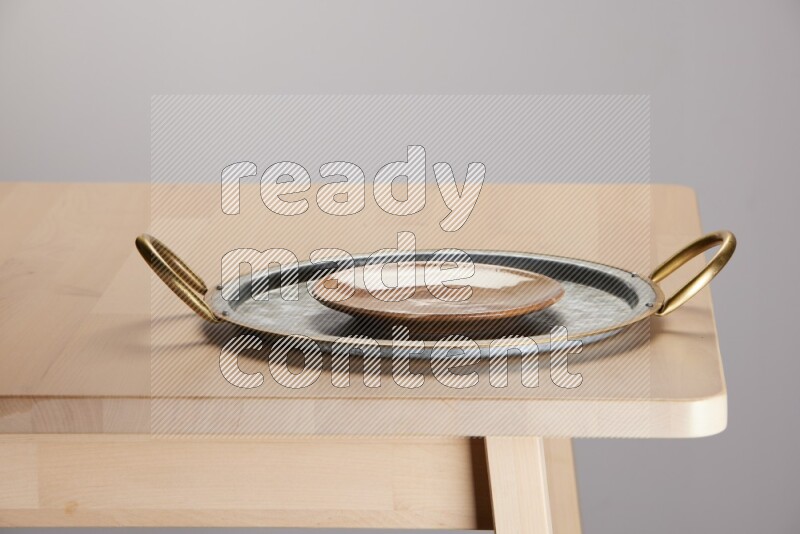 multicolored plate placed on a rounded stainless steel tray with golden handels on the edge of wooden table