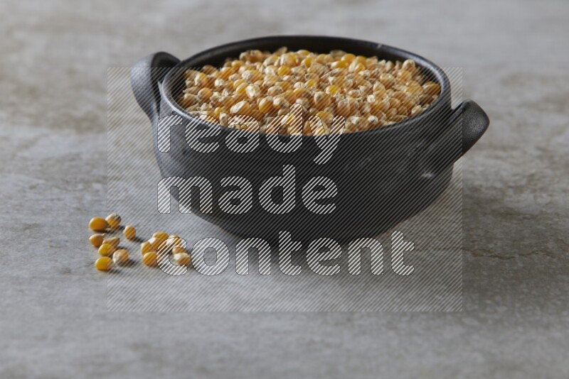 corn kernel in a black handheld ceramic bowl on a grey textured countertop