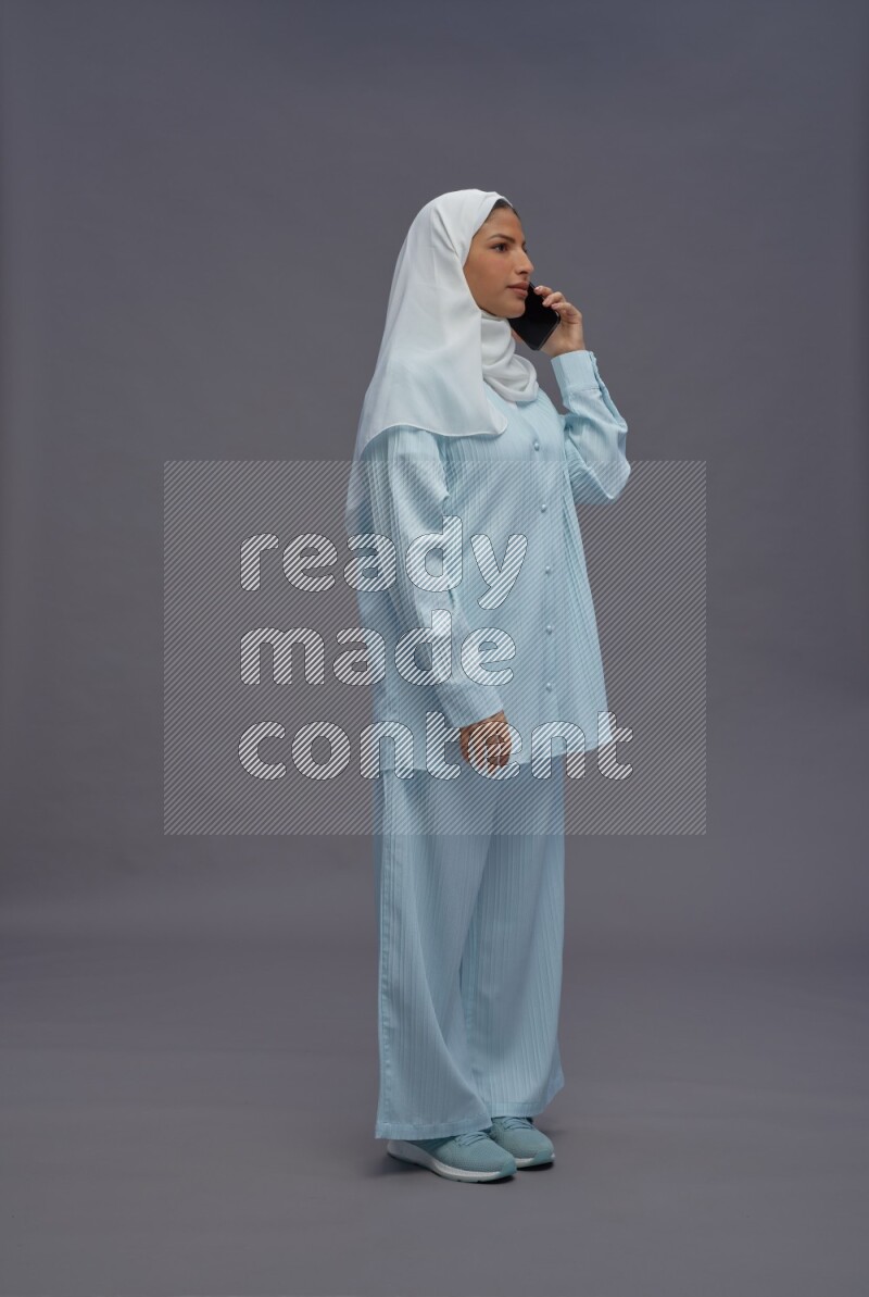 Saudi woman wearing hijab clothes standing talking on phone on gray background