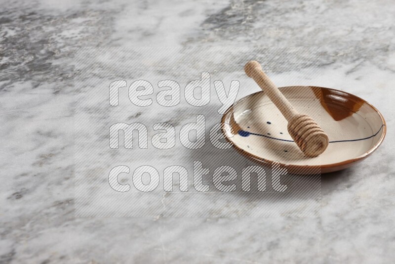 Multicolored pottery plate with wooden honey dipper in it on grey marble background