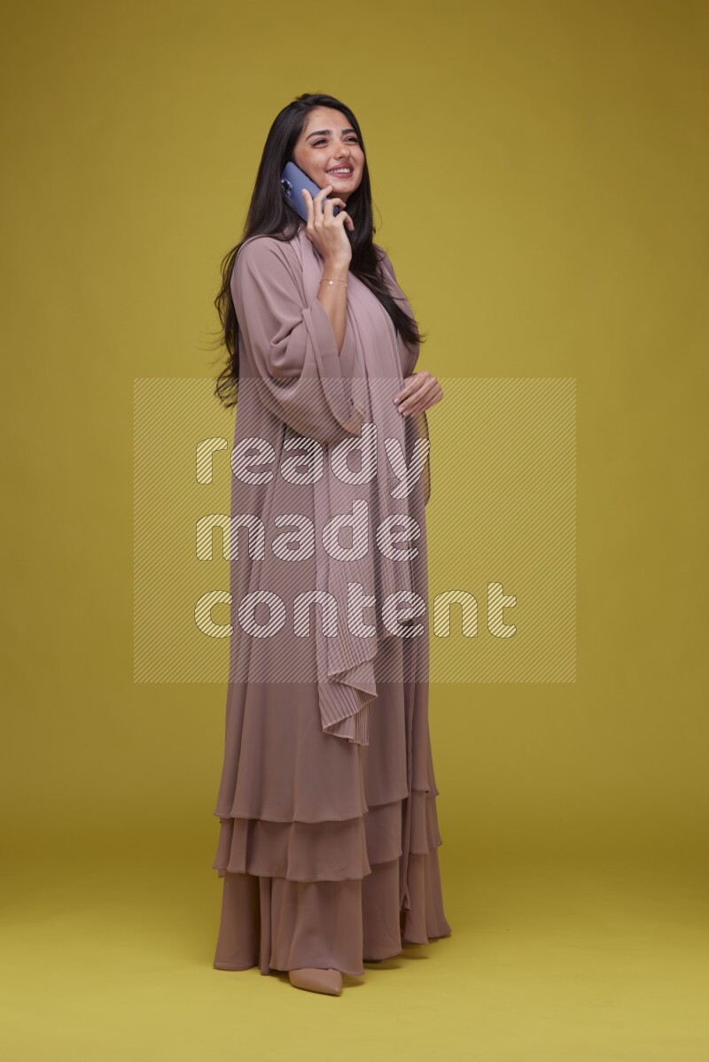 A woman Calling on a Yellow Background wearing Brown Abaya