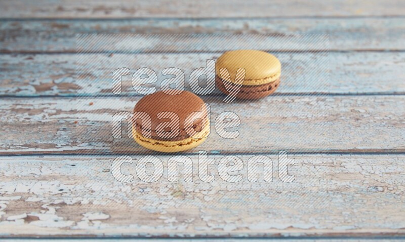 45º Shot of two Yellow and Brown Chai Latte macarons on light blue wooden background