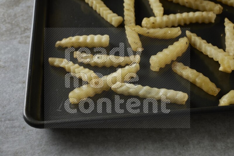 crinkle fries in a black stainless steel rectangle tray on grey textured counter top