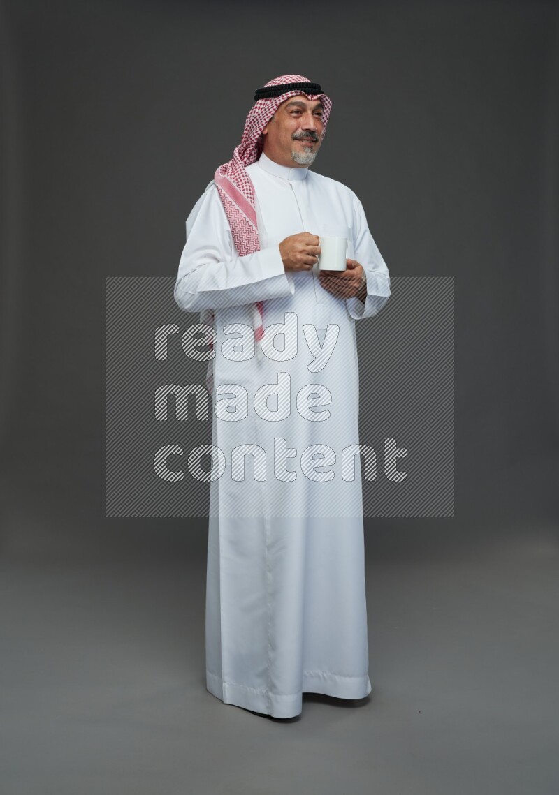 Saudi man with shomag Standing holding mug on gray background