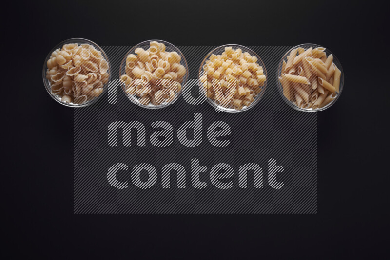 Different pasta types in glass bowls on black background
