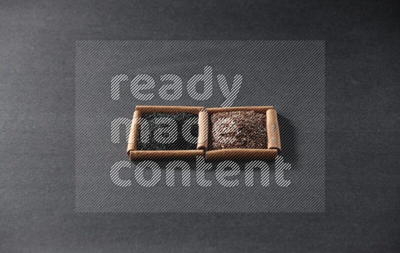 2 squares of cinnamon sticks full of flaxseeds and black seeds on black flooring
