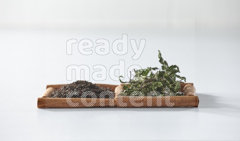 مربعان من أعواد القرفة ممتلئان بالشاي الأسود والنعناع المجفف علي خلفية بيضاء