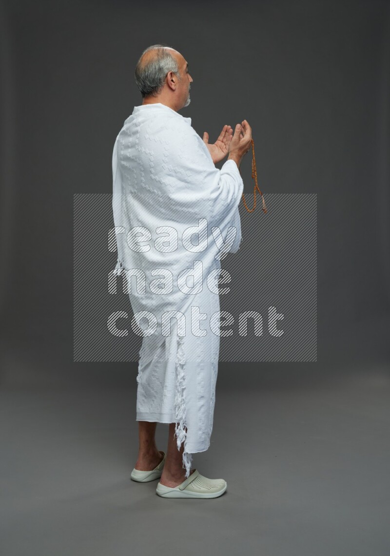 A man wearing Ehram Standing dua'a on gray background
