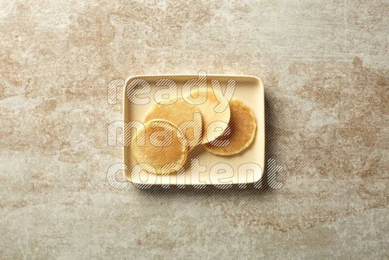 Four stacked plain mini pancakes in a rectangular plate on beige background