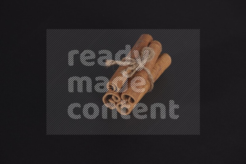 4 Cinnamon sticks stacked and bounded on black flooring