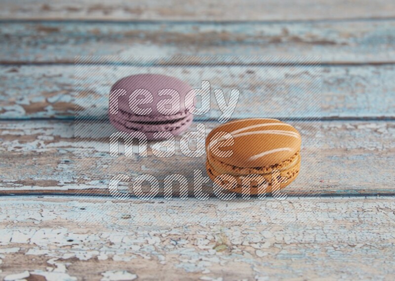 45º Shot of of two assorted Brown Irish Cream, and Purple Blueberry macarons  on light blue background