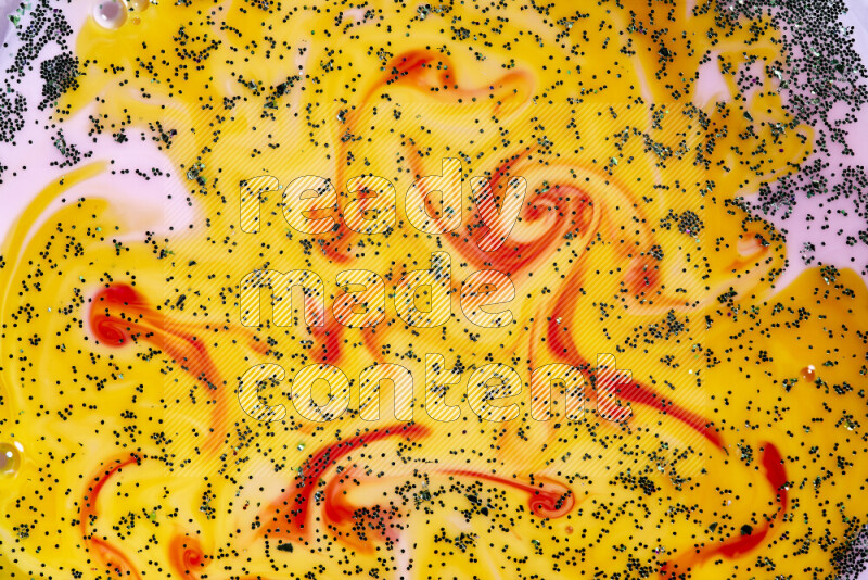 A close-up of sparkling green glitter scattered on swirling yellow, red and pink background