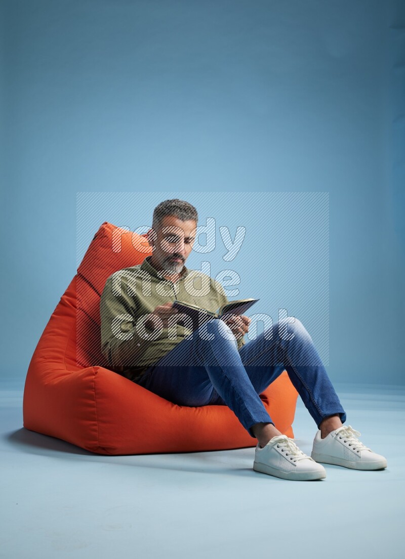 A man sitting on an orange beanbag and reading a book
