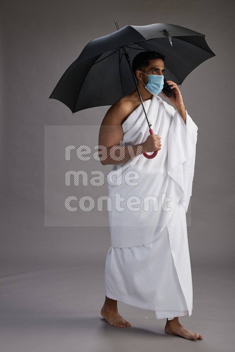 A man wearing Ehram and mask Standing holding umbrella on gray background on gray background