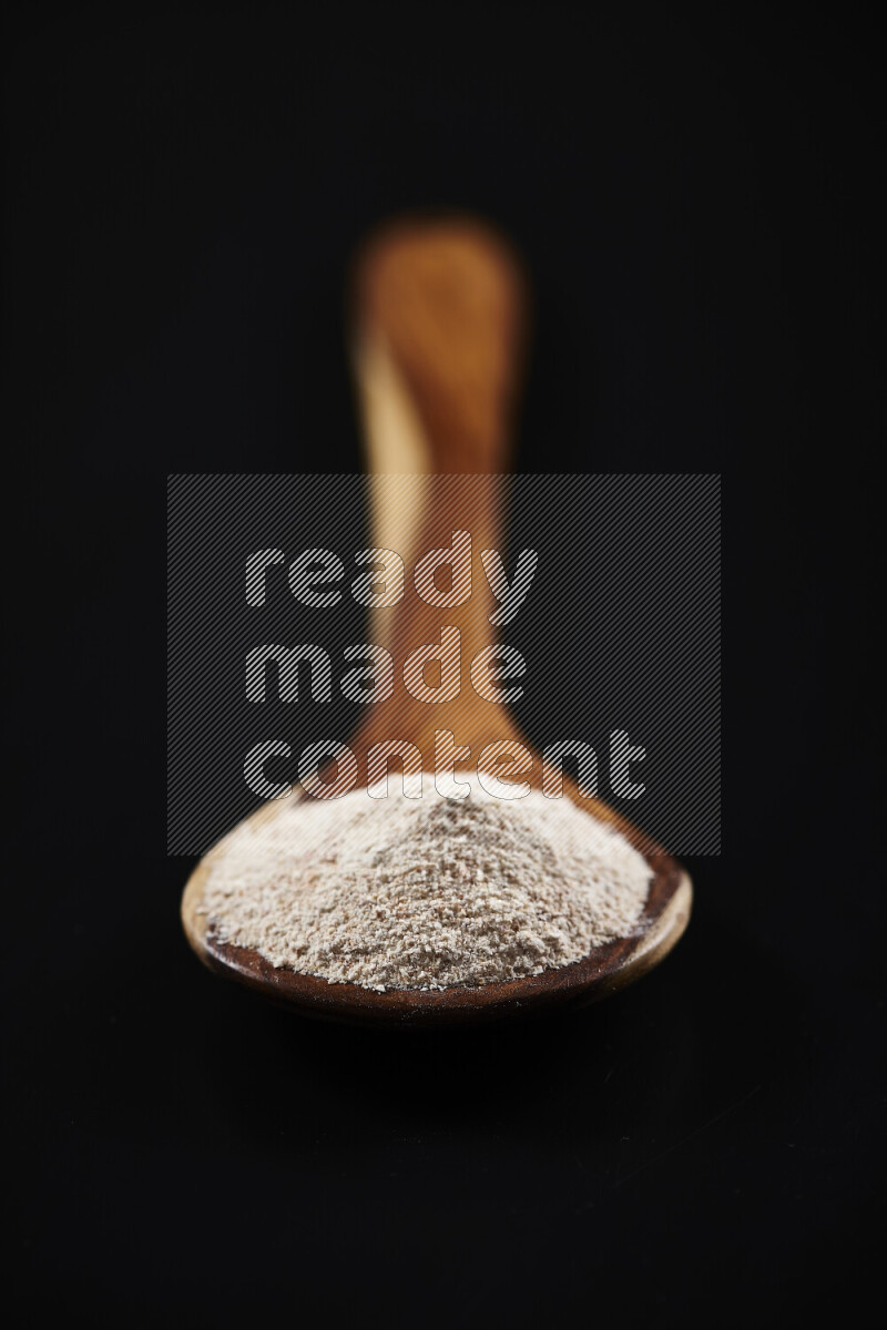 A wooden ladle full of onion powder on black background