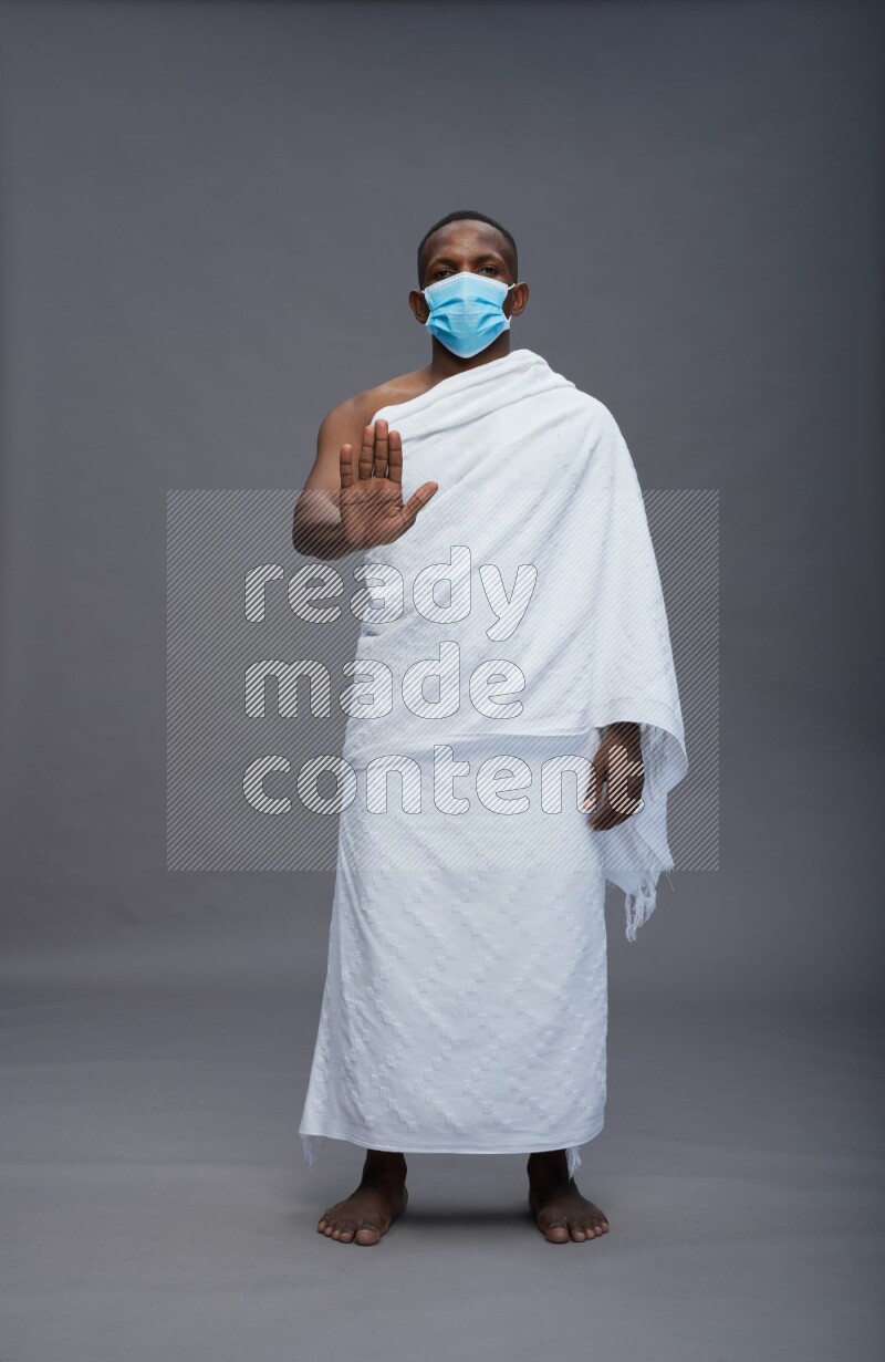 A man wearing Ehram with face mask Standing Interacting with the camera on gray background