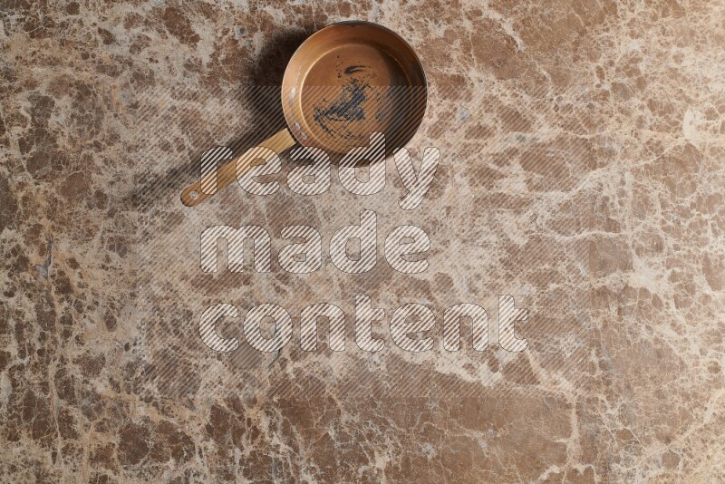A small copper pan on beige marble background