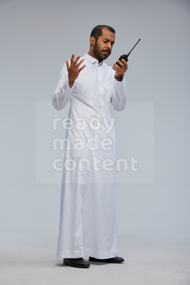 Saudi man Wearing thob standing holding walkie-talkie on Gray background
