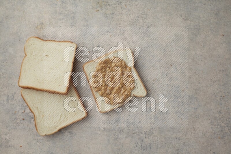 crunchy peanut butter on white toast and white toast slices on a light blue textured background
