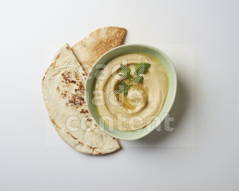 Hummus in a green plate garnished with parsley on a white background