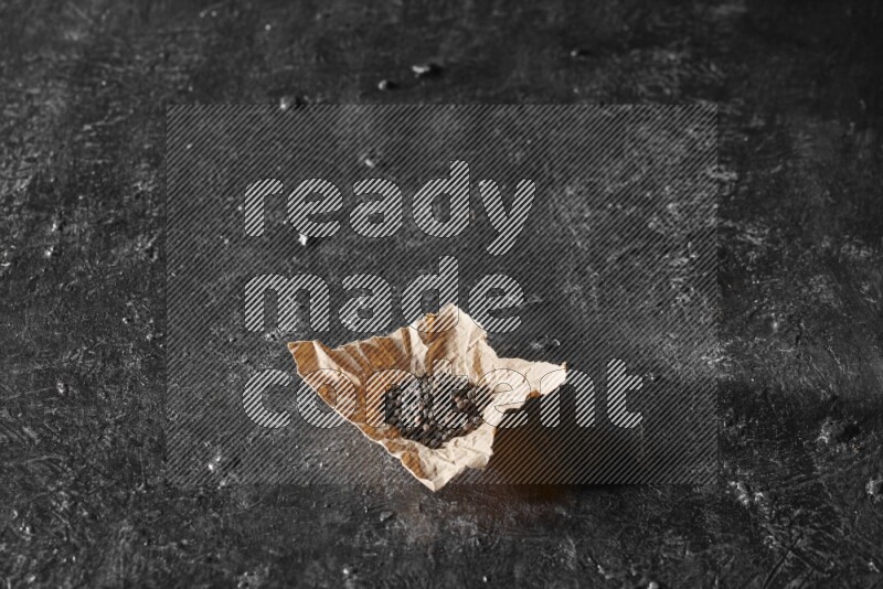 Black pepper beads on crumpled paper on a textured black flooring