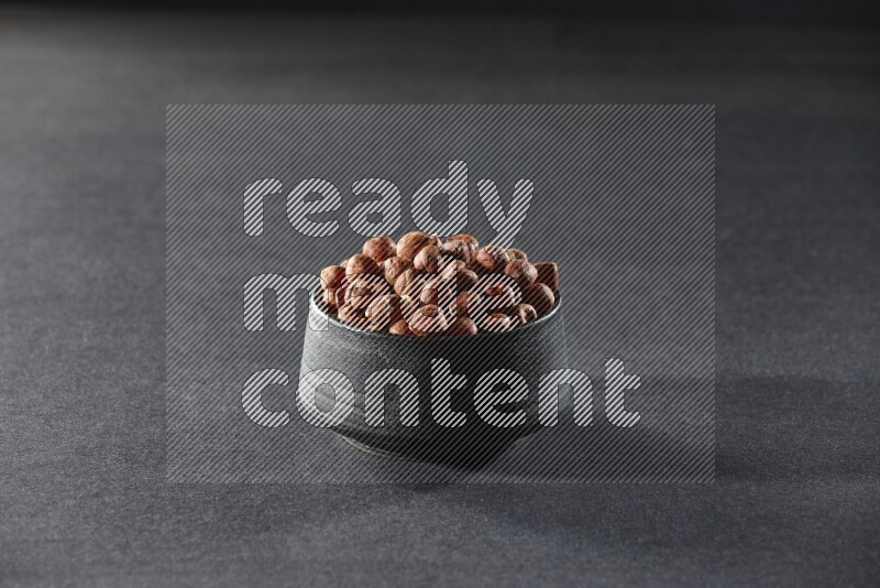 A black pottery bowl full of peeled hazelnuts on a black background in different angles