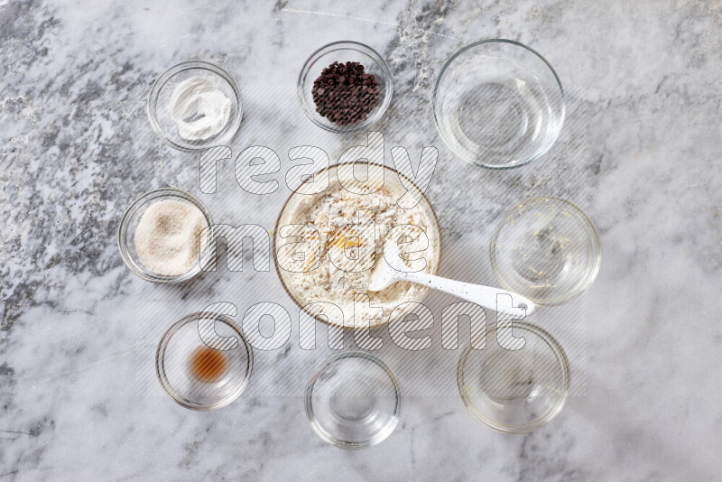 Cookies step by step with its ingredient, flour, butter, brown sugar, egg, vanilla extract, white sugar, chocolate chips and baking soda on grey marble background