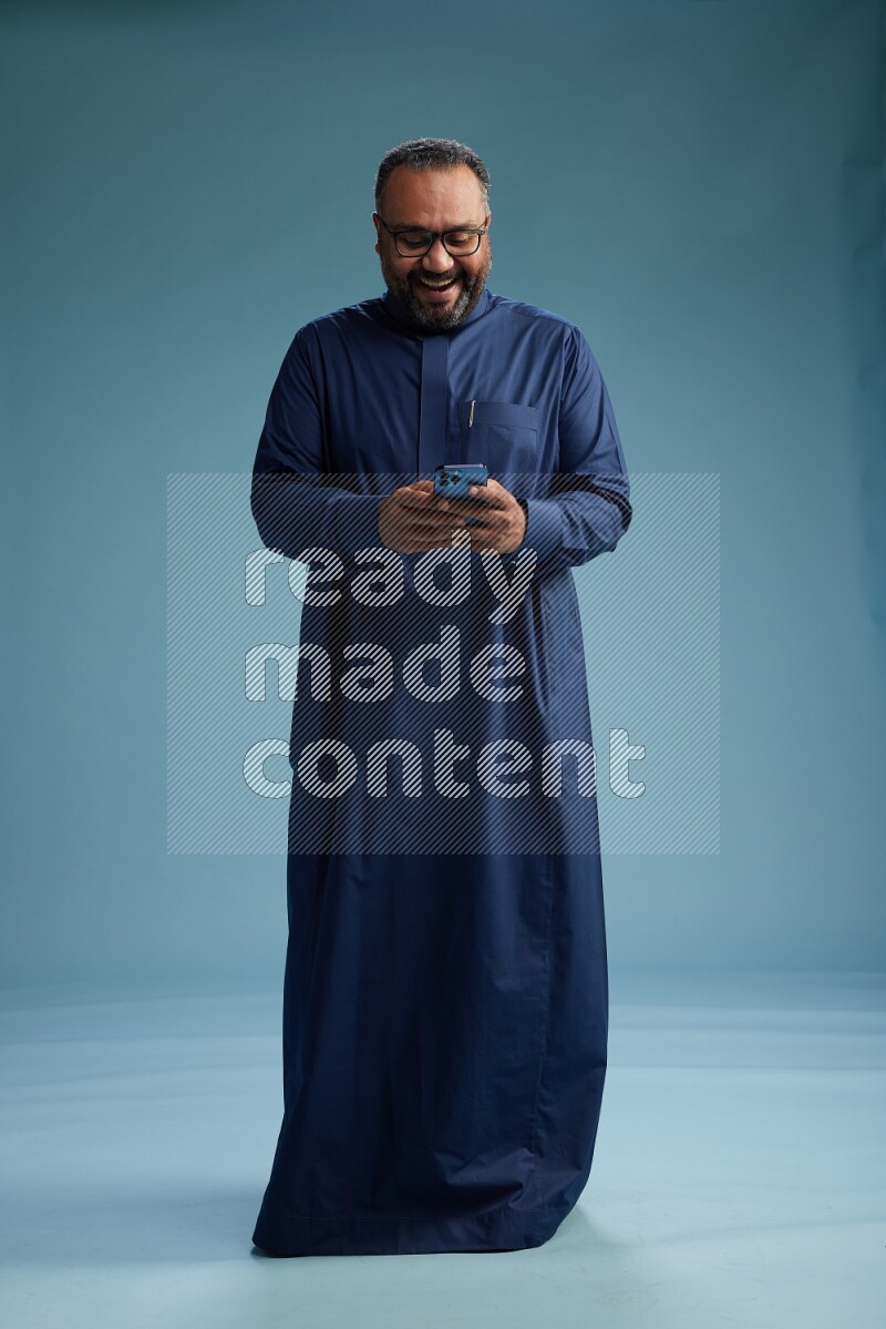 Saudi Man without shimag Standing texting on phone on blue background