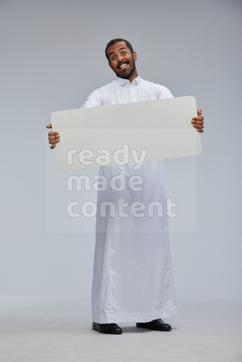 Saudi man wearing Thob standing holding board on Gray background