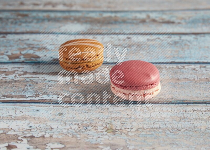 45º Shot of of two assorted Brown Irish Cream, and Pink Litchi Raspberry macarons on light blue background