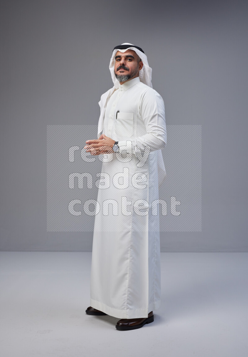 Saudi man Wearing Thob and white Shomag standing interacting with the camera on Gray background