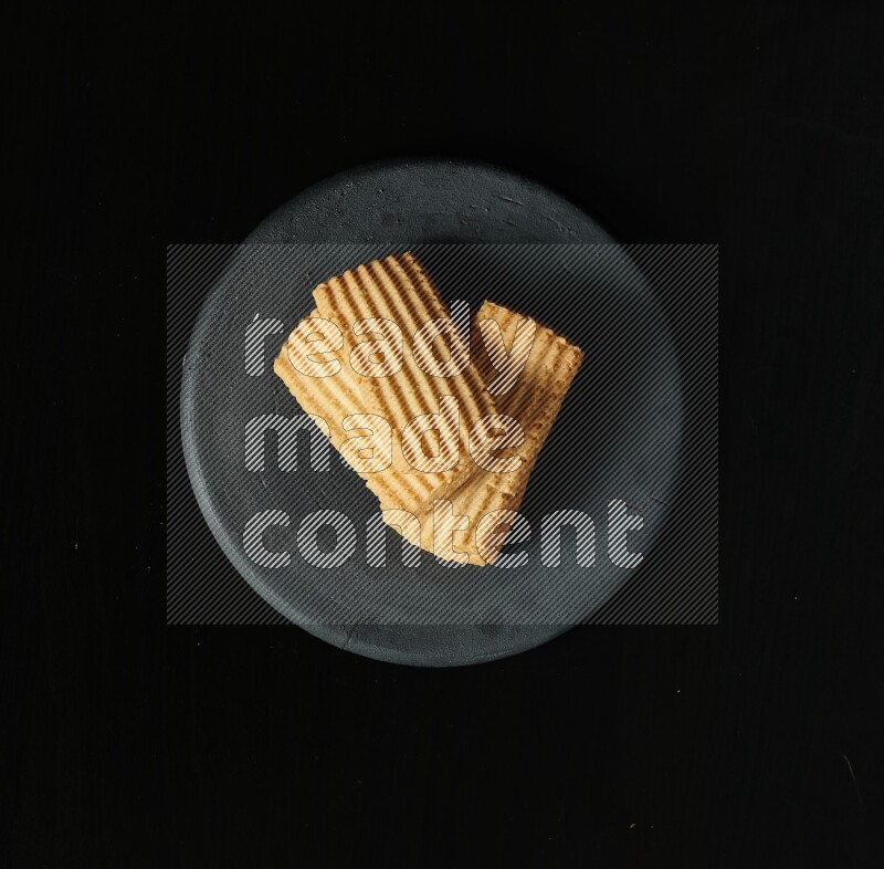 Golden biscuits in a black pottery plate on black background