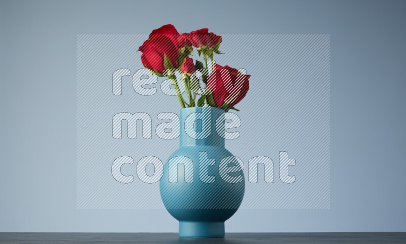An arrangement of vivid red roses in a blue vase on black marble background