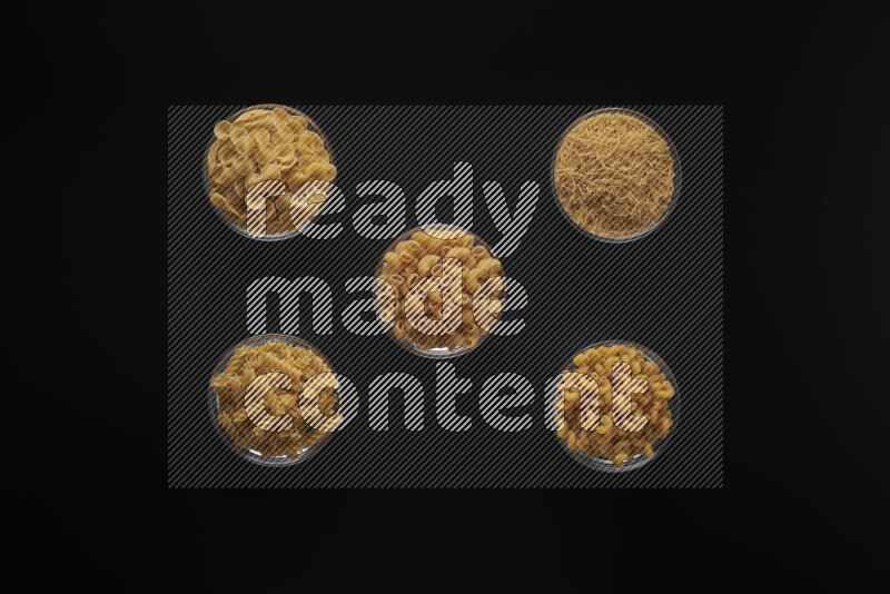 Different pasta types in 5 glass bowls on black background