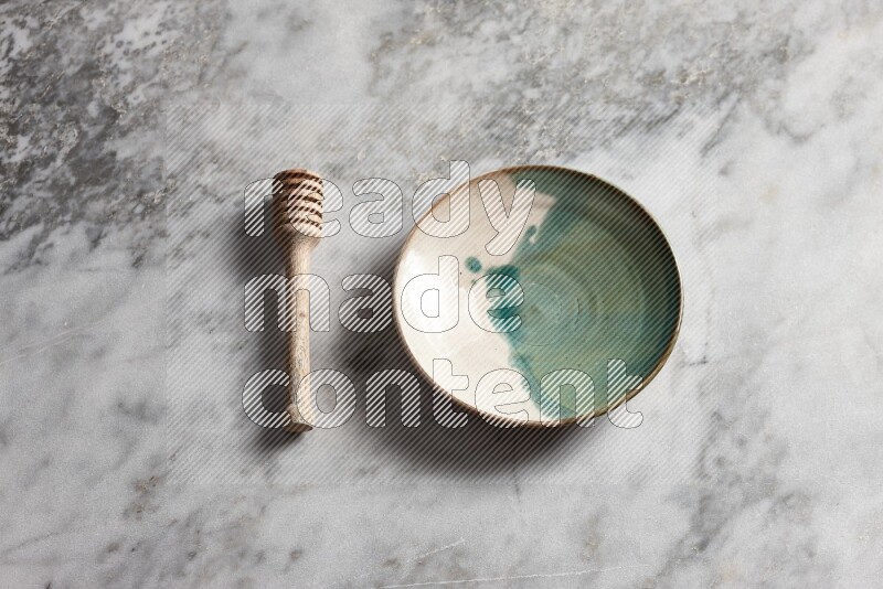 Multicolored pottery plate with wooden honey dipper on the side on grey marble background