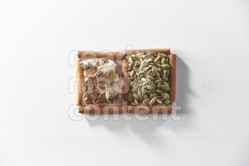 مربعان من أعواد القرفة ممتلئان بحبوب الهيل والزنجبيل المجفف علي خلفية بيضاء