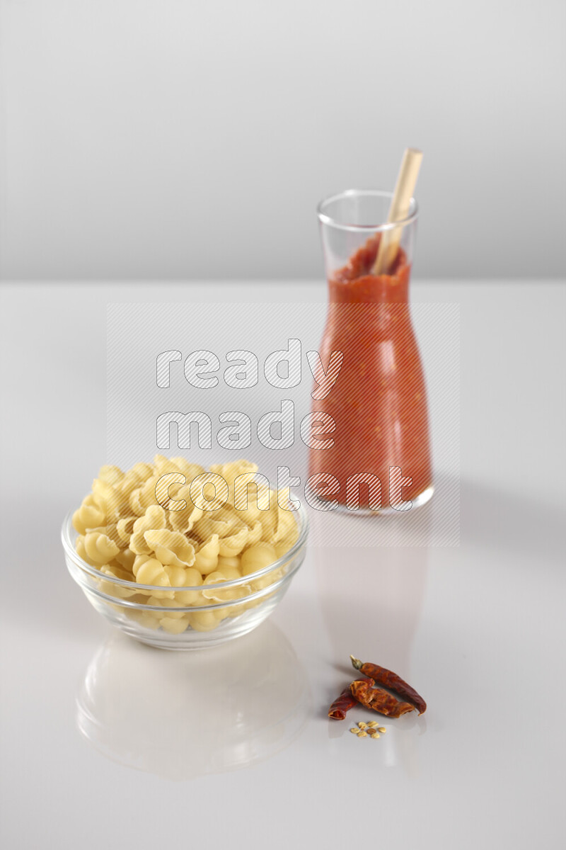 Raw pasta with tomatoe pasta with different ingredients such as cherry tomatoes, basil, garlic, bay laurel, cardamom, white pepper, black pepper, red chilis and wheat stalks on light grey background