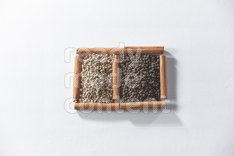 2 squares of cinnamon sticks full of black pepper and white pepper on white flooring