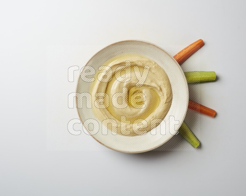 Hummus in a pottry plate garnished with olive oil on a white background