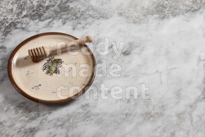 Decorative pottery plate with wooden honey dipper in it on grey marble background