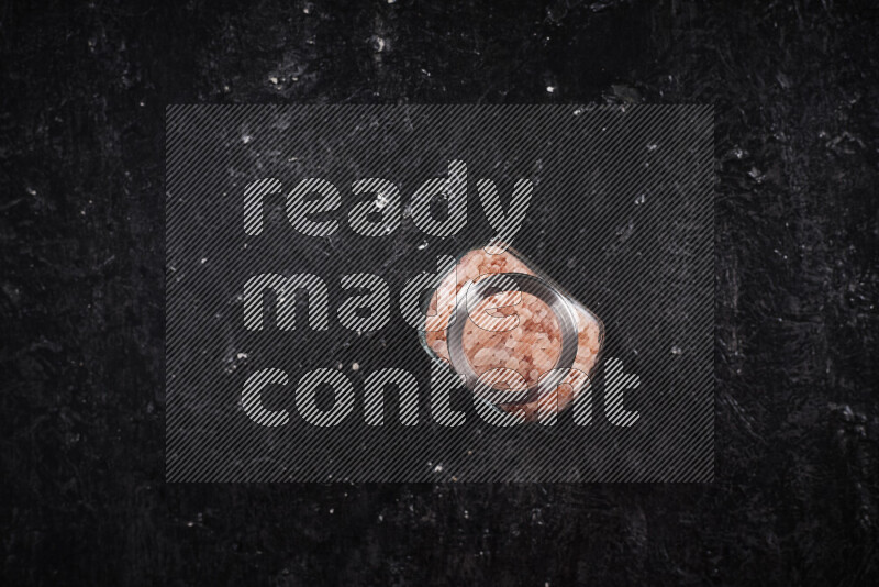 وعاء زجاجي ممتلئ بملح الهيمالايا الخشن على خلفية سوداء