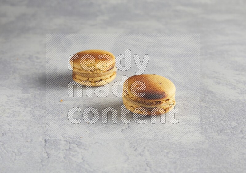 45º Shot of two Yellow Crème Brulée macarons on white  marble background