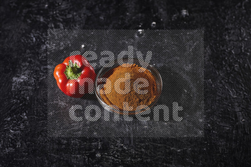 A glass bowl full of ground paprika powder on black background