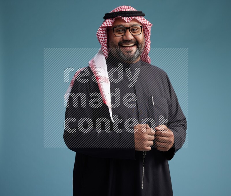 Saudi Man with shimag Standing Interacting with the camera on blue background