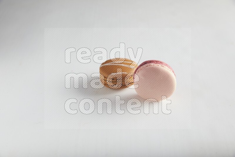 45º Shot of of two assorted Brown Irish Cream, and Pink Litchi Raspberry macarons on white background