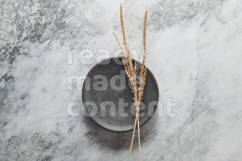 Wheat stalks on black pottery plate on grey marble background