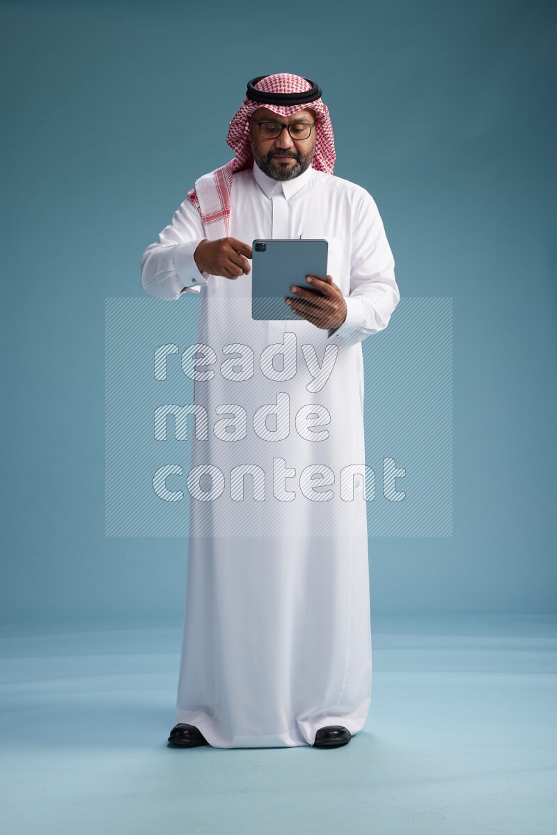 Saudi Man with shimag Standing holding a tablet on blue background